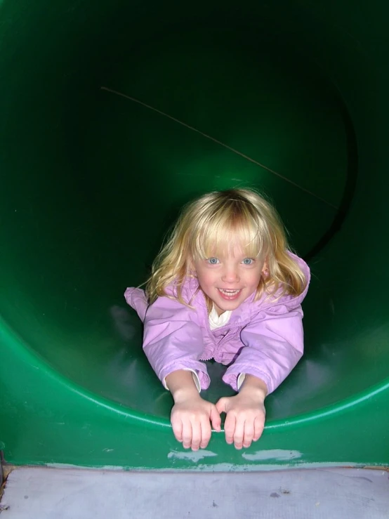 the girl is standing in a green playground tunnel