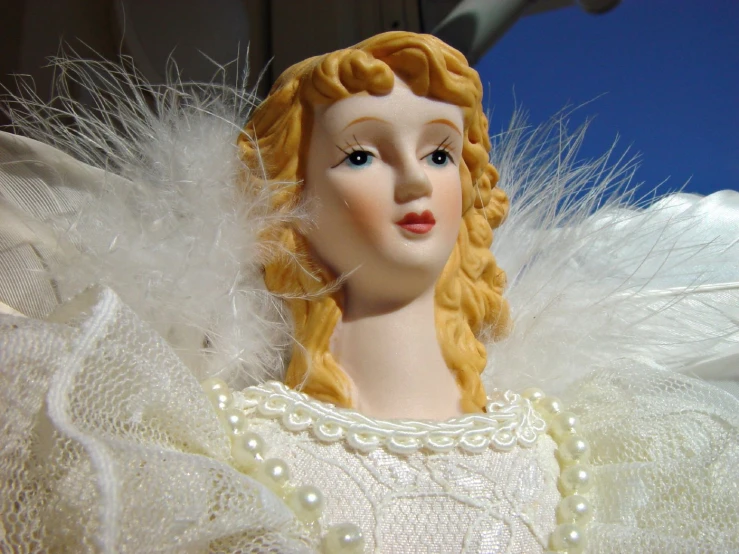 an angel doll with white feathers and a pearl necklace