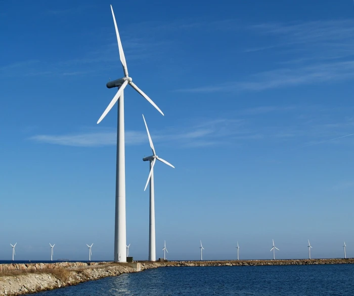 a group of windmills stand in the water beside the shore