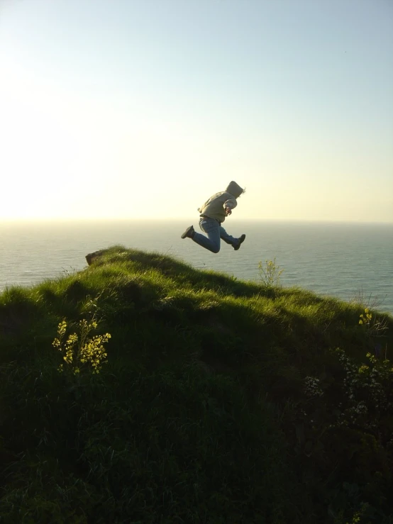 a man falling over a grassy hill next to the ocean
