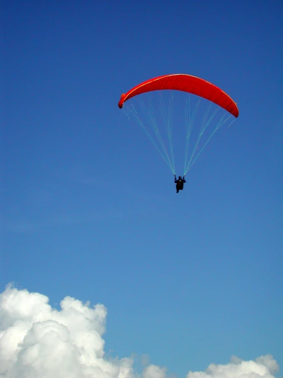 a para glider flying through a cloud filled blue sky