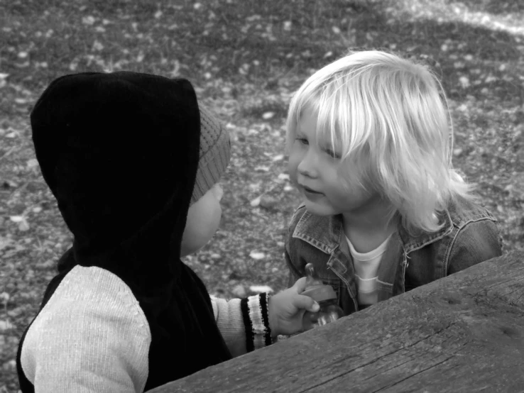 two young children wearing a hooded jacket talking