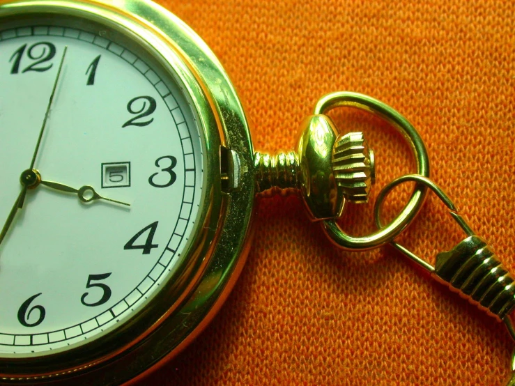 a close up of a gold pocket watch on orange fabric