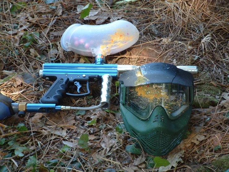 a blue paintball gun and mask sit in the grass