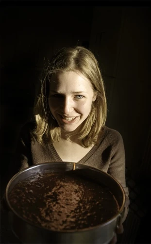 a smiling lady in the shadows holding a chocolate pan