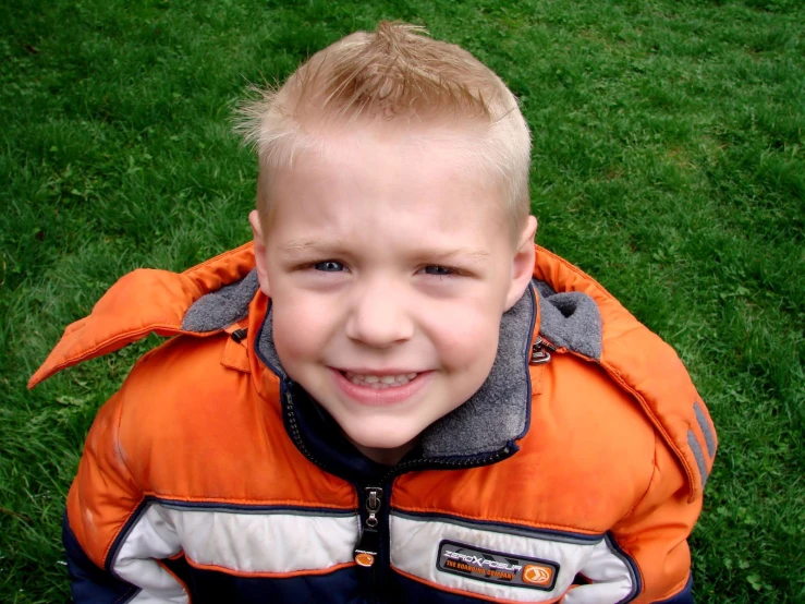 a  in an orange jacket and green grass smiling at the camera