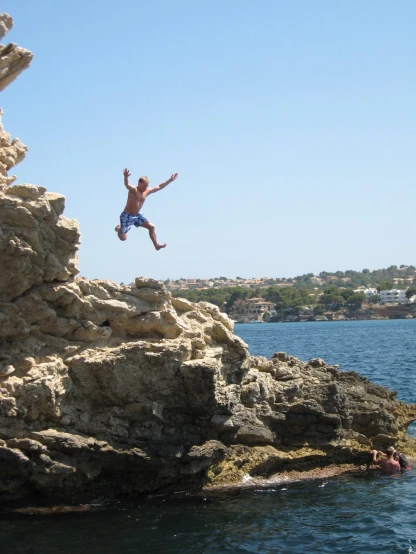 man jumping off cliff into the water on sunny day