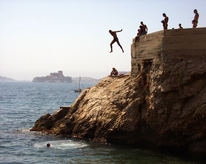 men jumping off rocks in the water off a cliff