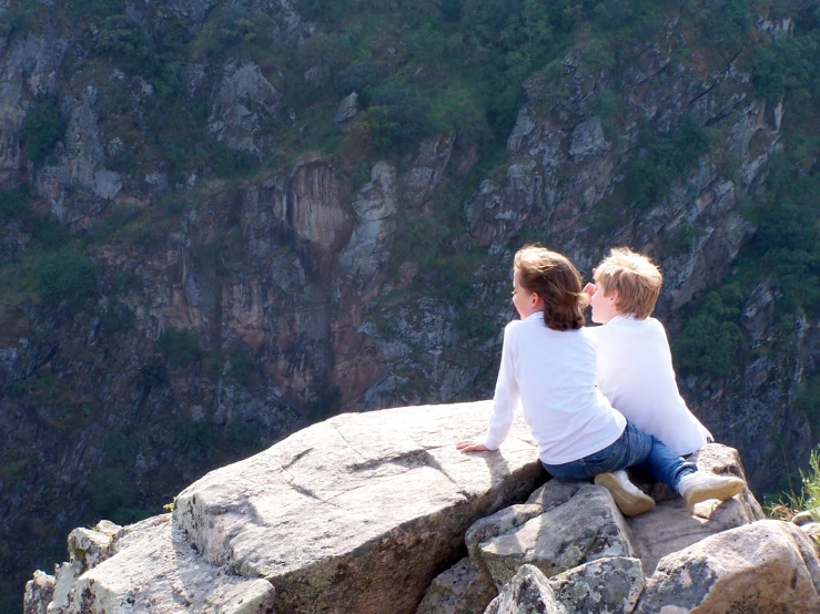 two children sitting on a rock near the mountains