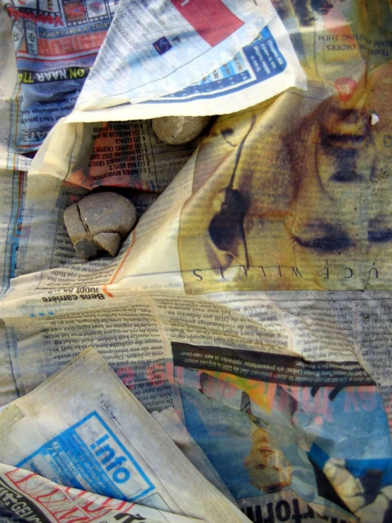 newspapers and rocks laying on the floor with a torn newspaper page covering them