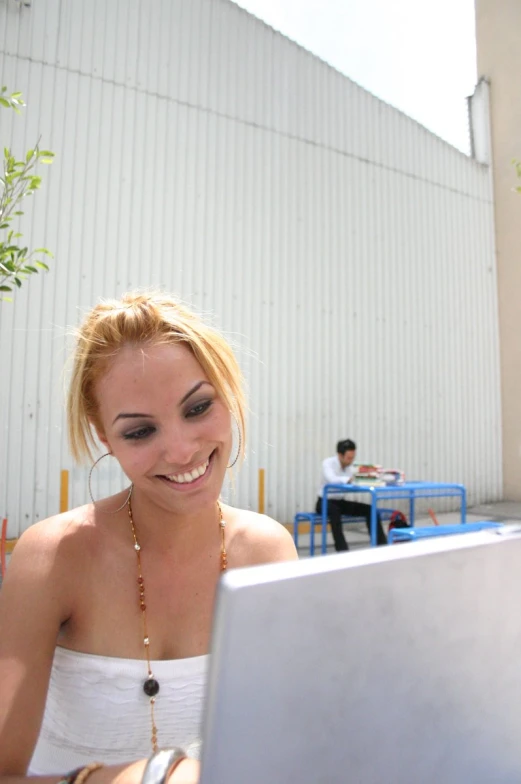 a woman smiles while looking at the screen on her laptop