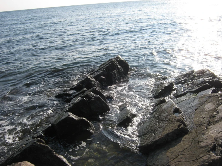 rocks sticking out from the ocean with a sun shining above them