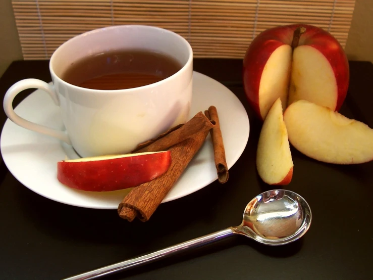 a cup of tea next to apples on a black table