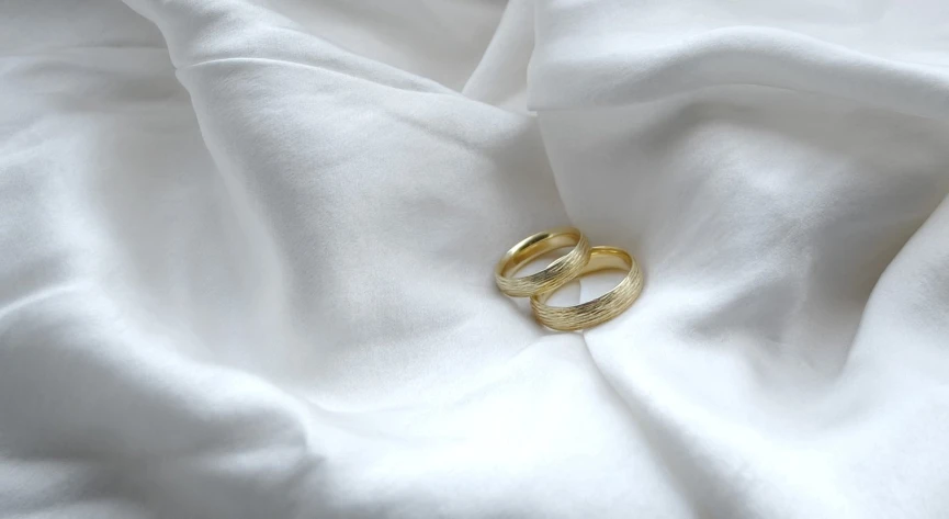 two wedding rings are sitting on white fabric