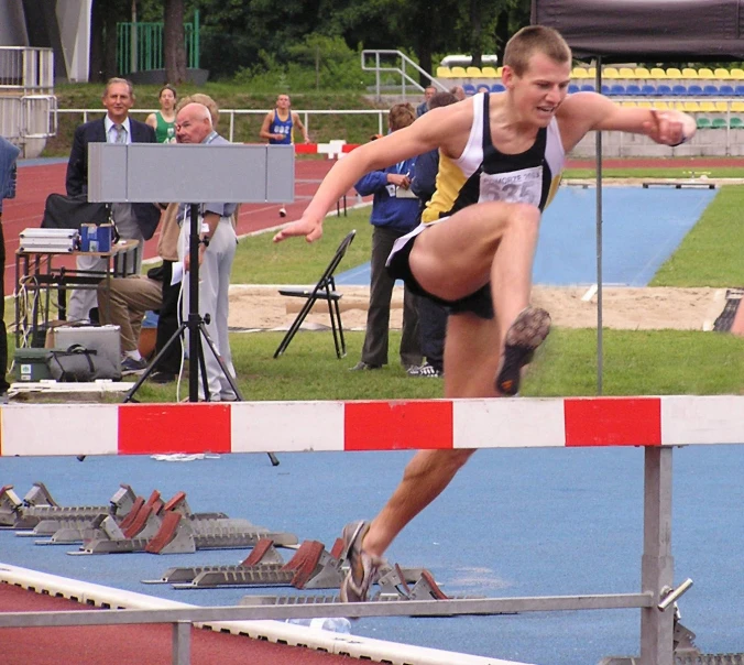 an athletic man jumping over a hurdle on top of a blue surface