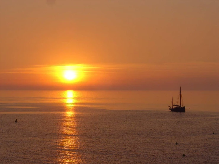 the sun setting over the water and a boat out on it