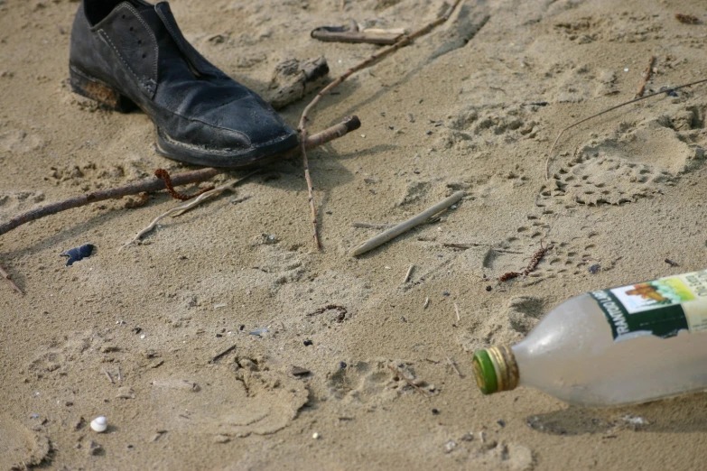 a bottle of wine sitting on the sand next to a pair of shoes