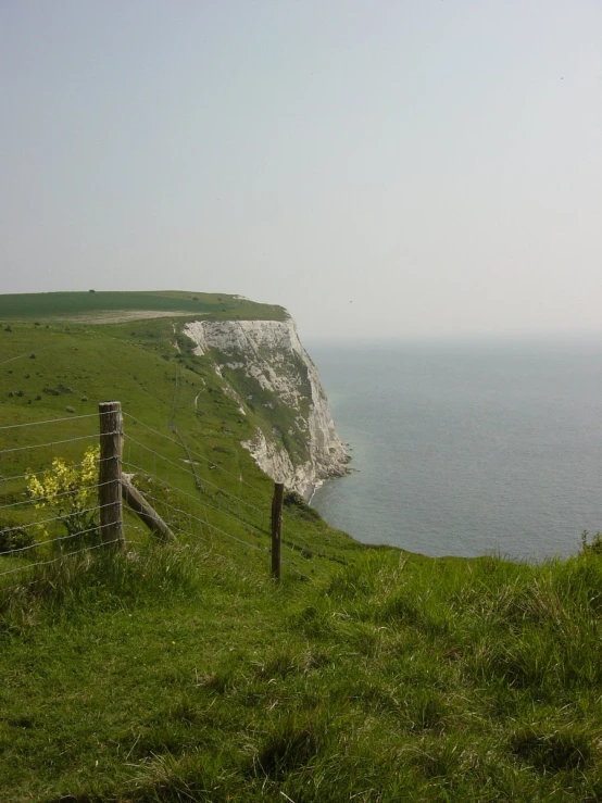 an empty hill with grass and a fence overlooking the ocean