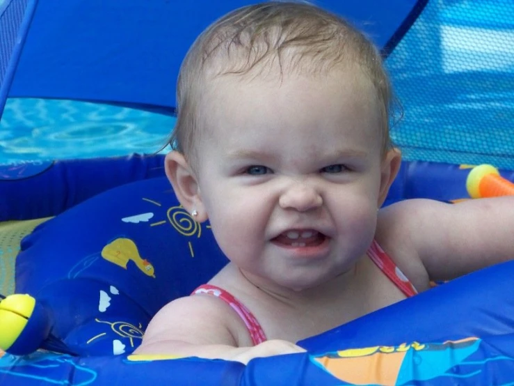 an adorable baby playing in a pool, wearing blue swim suit
