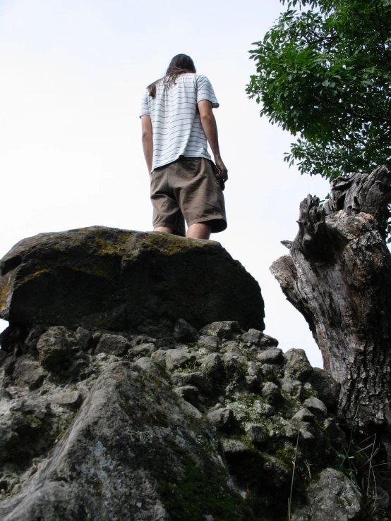 a young person stands on the edge of a rock and looks up at a cliff