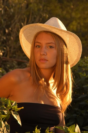 a close - up of a young woman with a hat standing in the bush