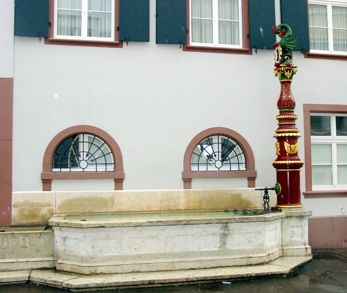 a fountain in front of a white building with shutters open