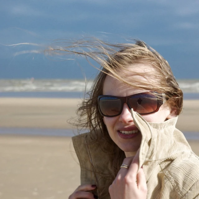 a girl with sun glasses standing in front of the ocean