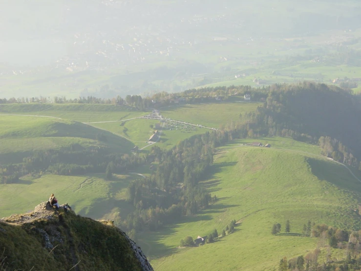 a man sits on a grassy hill with a view of the countryside