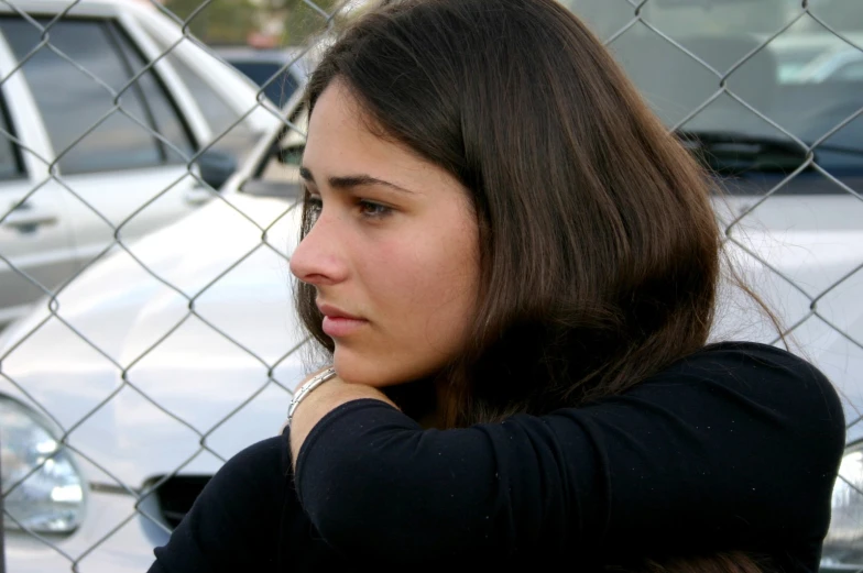 woman holding her arm behind her head in front of a fence and cars