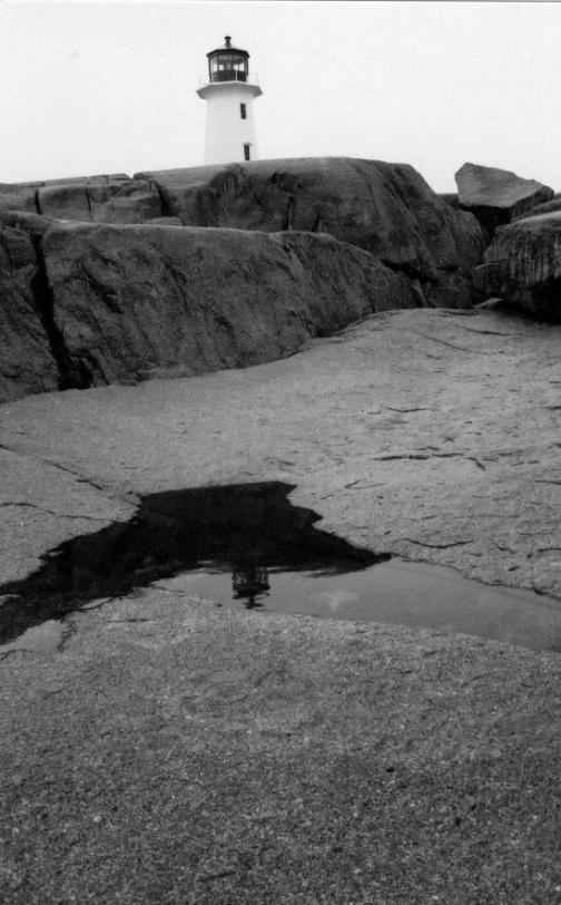 the black and white lighthouse reflects in the water