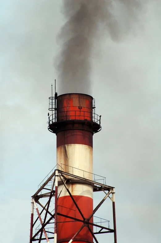 an old red and white lighthouse with smoke pouring out of it