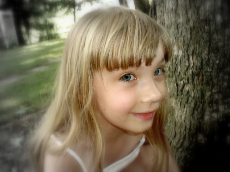 a little girl posing for a picture in front of a tree