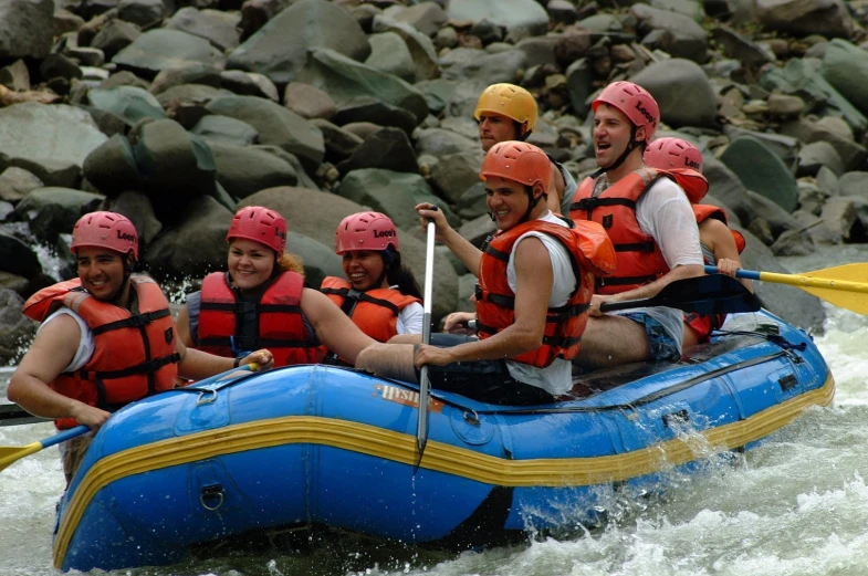 several young men and one girl, wearing helmets, white rafting on the river