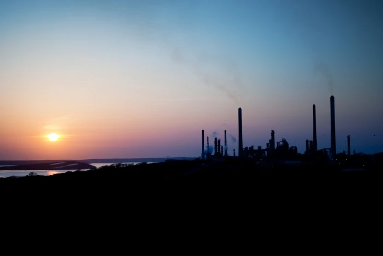 a factory field with smoke stacks and the sun in the distance