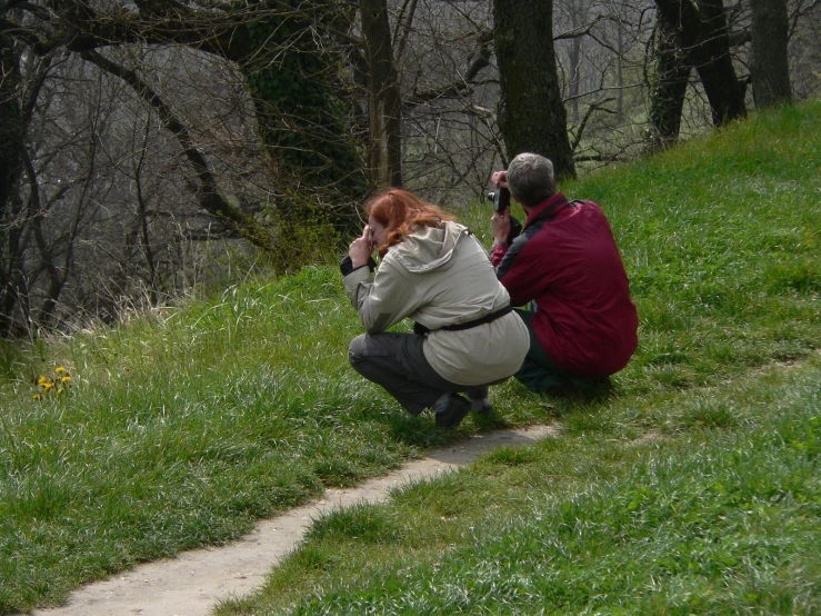 a couple takes pictures as they crouch down in the grass