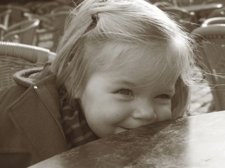 little girl is leaning on table smiling in sepia