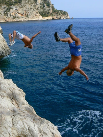 the two people are diving off a cliff into the water