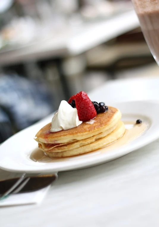 plate topped with a pile of pancakes with whipped cream and berries