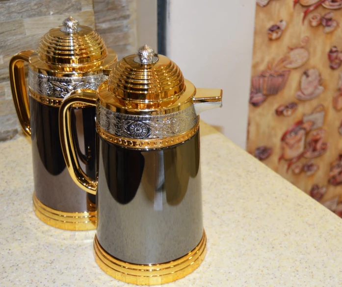 two silver and gold coffee pots on top of a counter