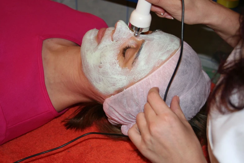 a woman in pink shirt using facial mask on another person