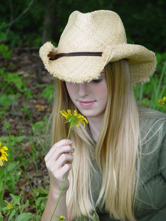a beautiful young woman holding a flower on a field