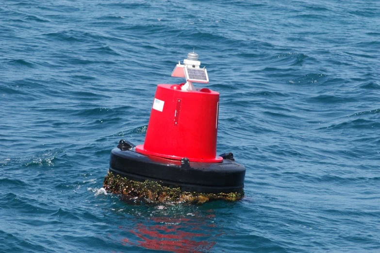 a red and black buoy floating in blue water