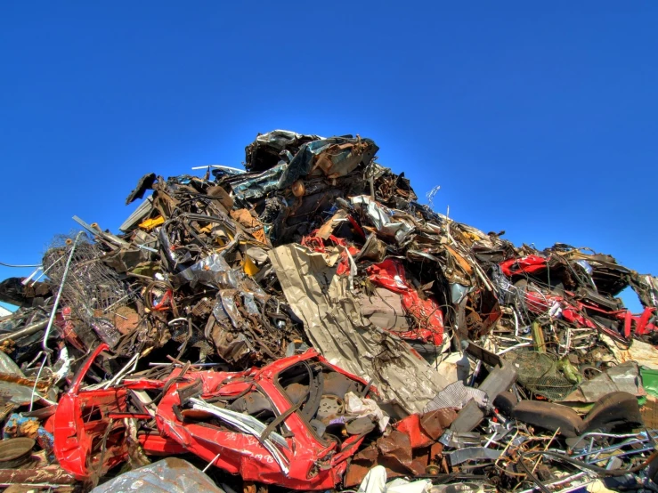 large pile of crushed car parts against a blue sky