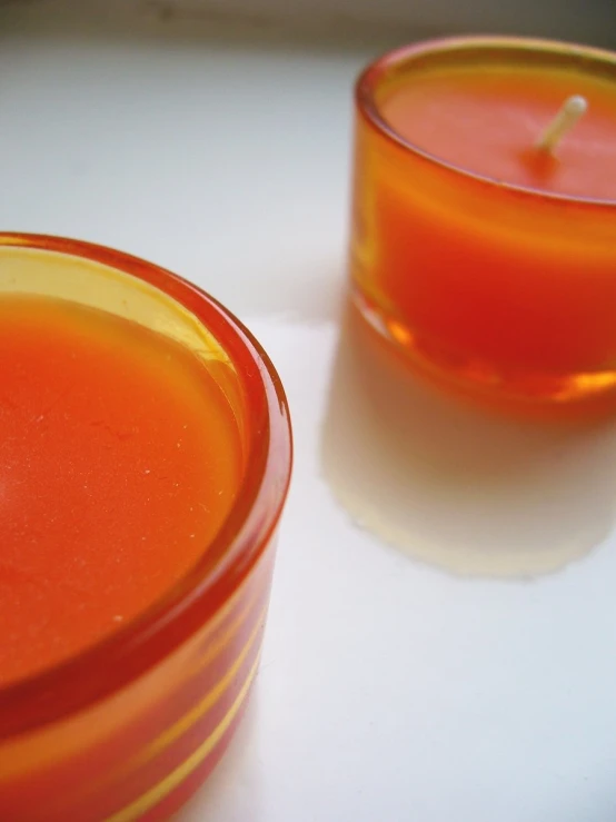 an orange colored candle is placed next to a cup with the lid down