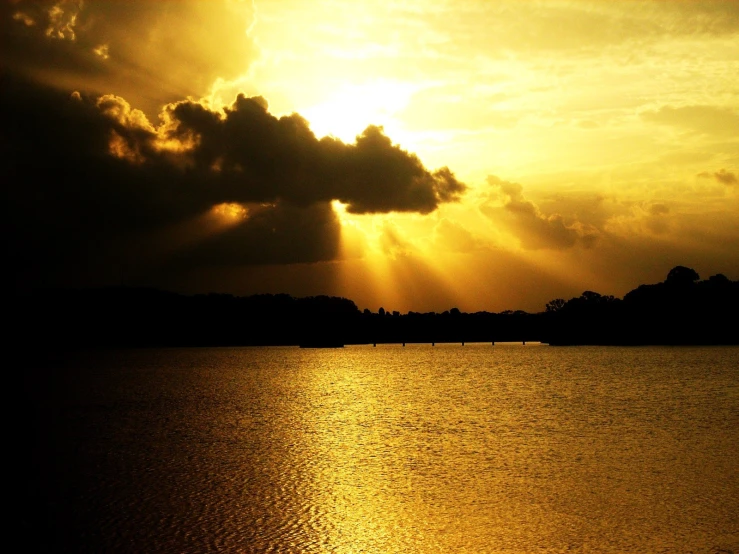 the sun shining through clouds over a lake