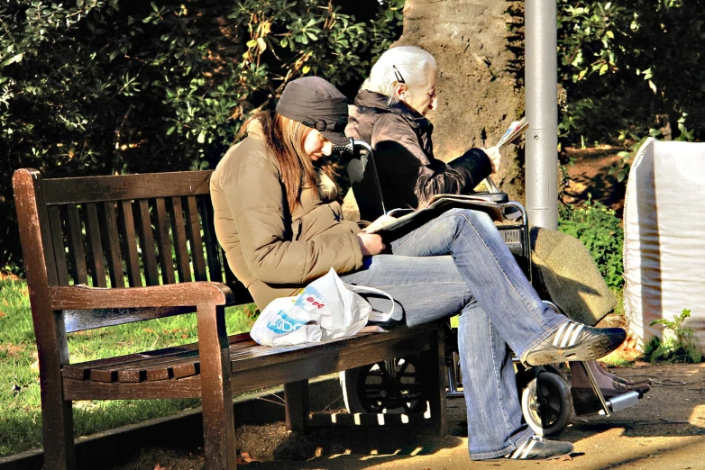 two people sitting on a park bench looking at a phone