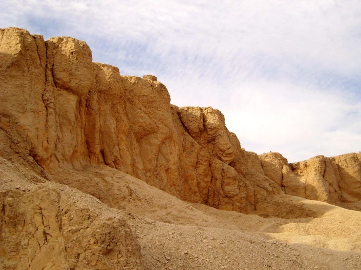 a rocky cliff is in the desert near a blue sky