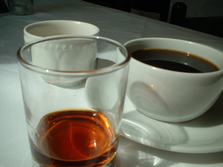 two white cups on a white plate and a glass full of espresso coffee