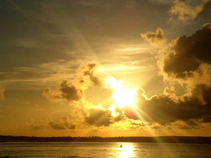 the sun is shining through clouds over a body of water