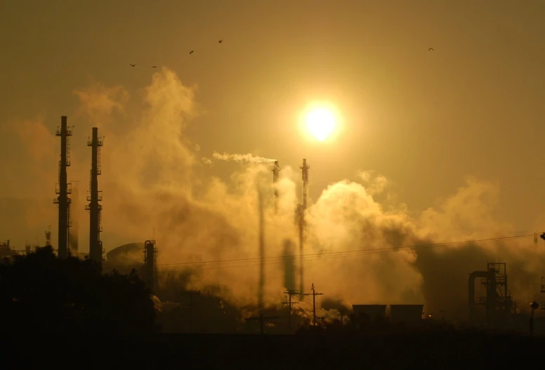 a factory smoking at sunset with the sun low in the sky